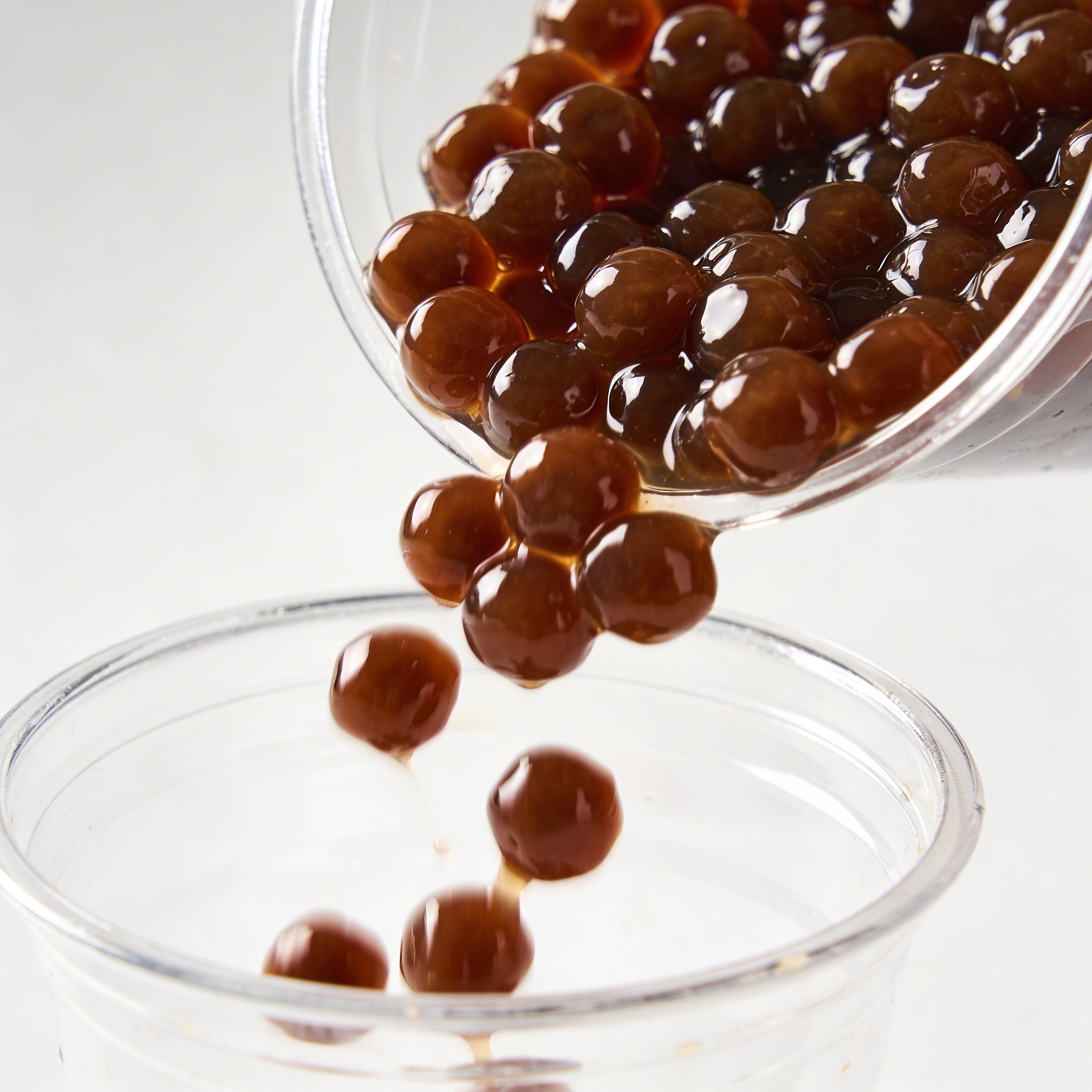 Clear glass bowl with dark brown tapioca pearls on a white background