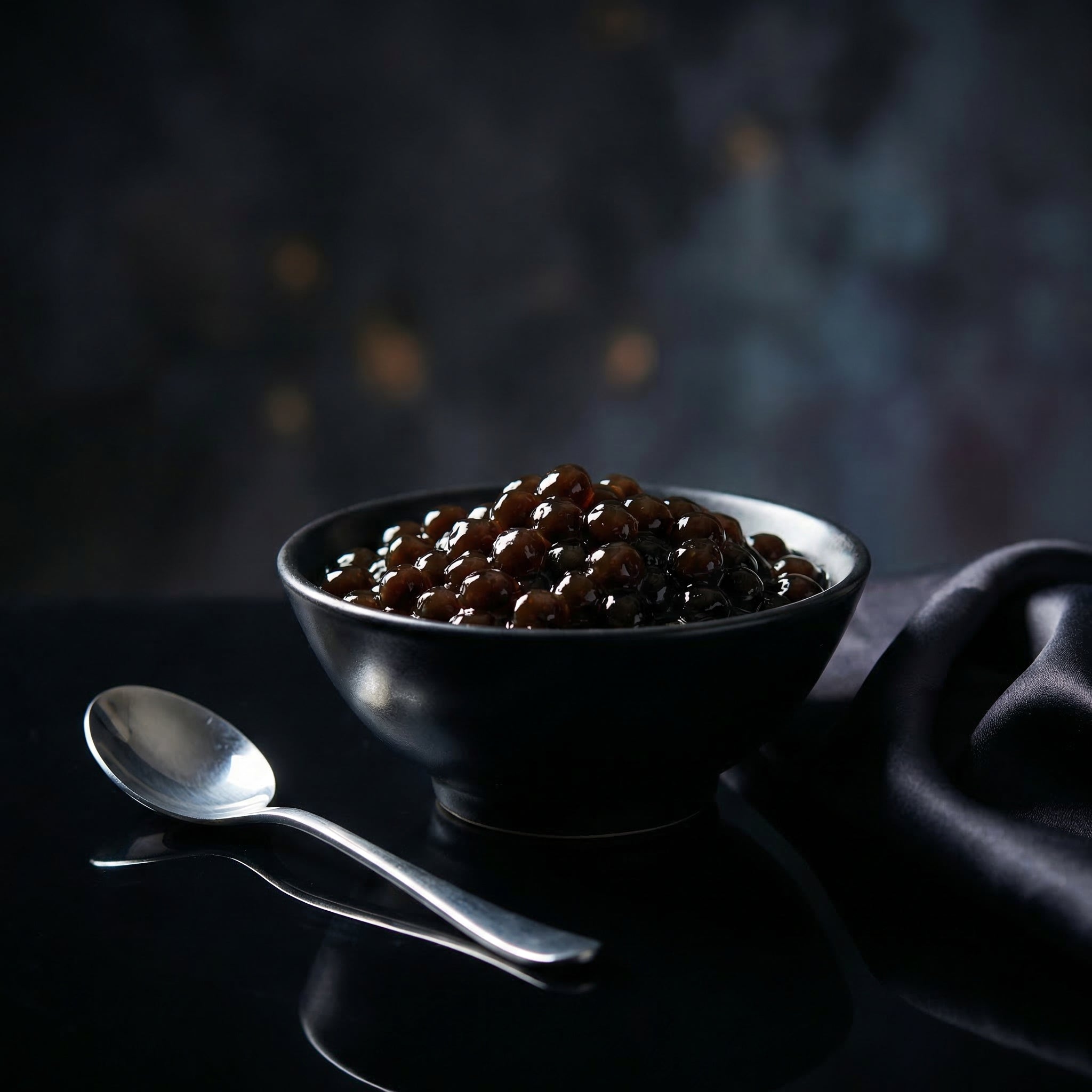 Black bowl filled with cooked tapioca pearls a dark surface with a spoon.