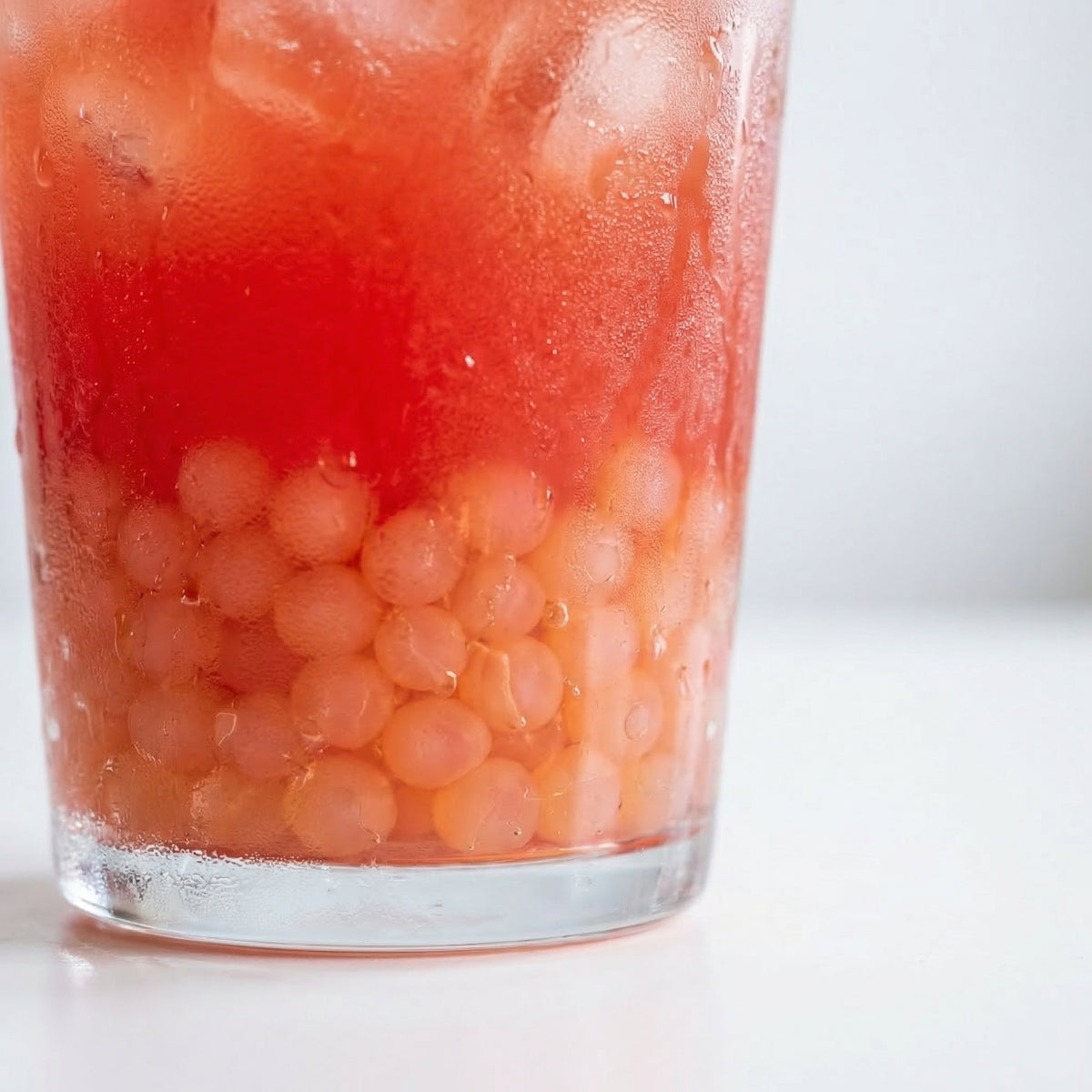 Glass of red fruit punch with ice and watermelon pearls on a white background